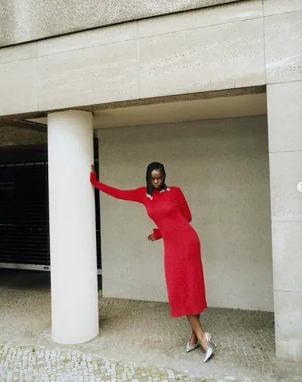 A model in a red midi dress beside a pale concrete column.