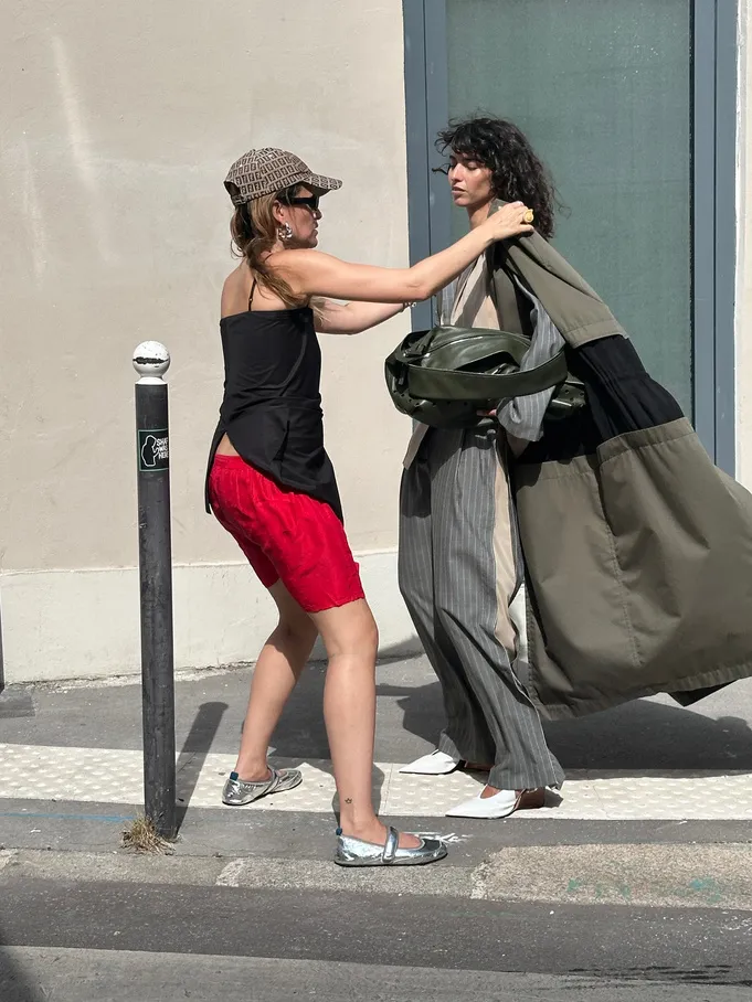 Two stylists carrying garment bags along a street on a shoot day.